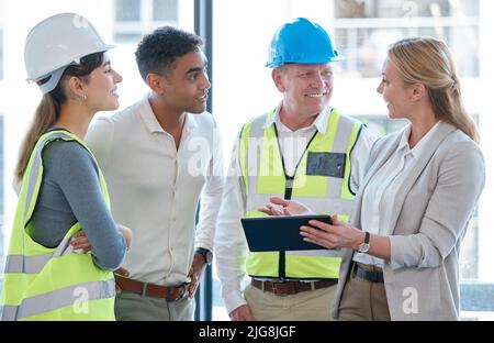 Building plans are digital now. Cropped shot of four construction workers looking over a tablet while having a meeting. Stock Photo