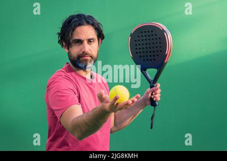 Monitor of padel holding black racket with yellow tennis ball in the hand. Class to student on outdoor tennis court. Man paddel player playing a match Stock Photo