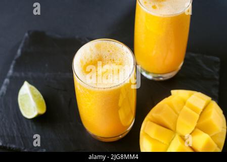 Mango and lime juice nectar. A refreshing summer drink on a black background. Bright yellow and black colors. Mango juice on a dark background. Summer Stock Photo