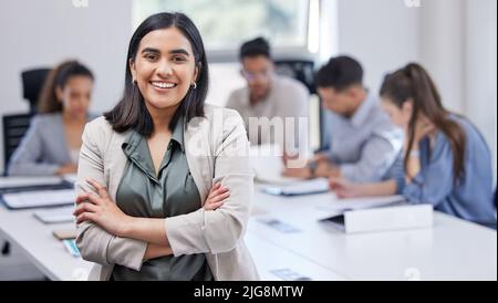 A team of hard workers. Shot of a young businesswoman standing with her arms crossed in an office at work. Stock Photo