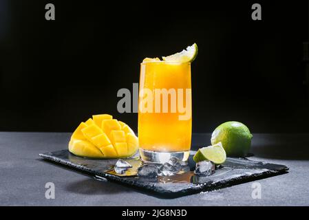 A Mexican smoothie drink made from mango, chili peppers, salt, and lime. A refreshing summer smoothie on a black background of bright orange. Stock Photo