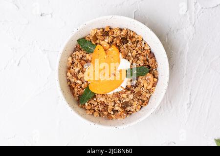 Bowl of homemade granola with yogurt and fresh peach on white background from top view. Superfoood Stock Photo