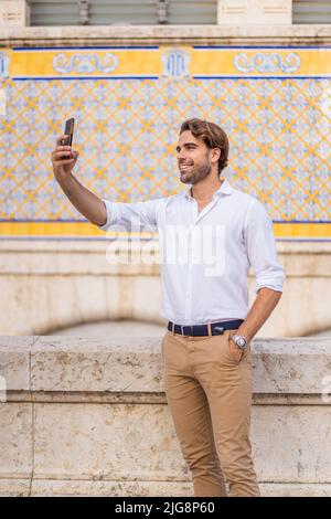 Young caucasian man with blond hair dressed in casual clothes taking a selfie with his cell phone in the city center of Valencia at Mercado Central. Stock Photo