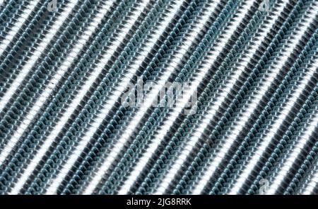 The threaded bolts are stacked side by side to create an abstract structure. Enlarged metal threaded rods. Abstract metal background. Stock Photo