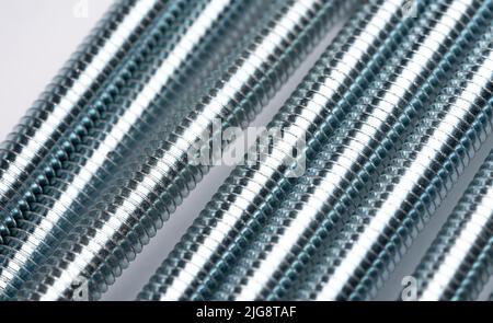 The threaded bolts are stacked side by side to create an abstract structure. Enlarged metal threaded rods. Abstract metal background. Stock Photo