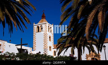 Spain, Canary Islands, Fuerteventura, Betancuria, Old Capital, Old Town, steeple of the church Iglesia de Santa Maria de Betancuria, palm trees in the foreground, blue cloudless sky Stock Photo