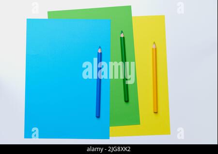 three colored pencils on blue, green and yellow paper Stock Photo