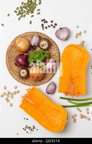 Two halves of pumpkin. Mushrooms, onions and broccoli on wicker plate. Pumpkin seeds on the table. Flat lay. White background. Stock Photo