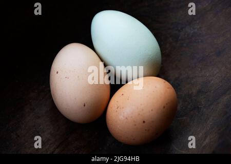 Three fresh colorful chicken eggs in a rustic wooden bowl. Stock Photo