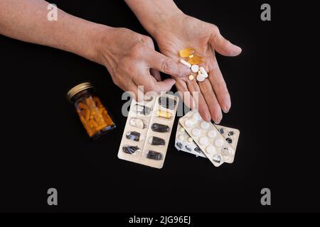 Close-up, a large number of different pills on a black background in the hands of an elderly woman Stock Photo