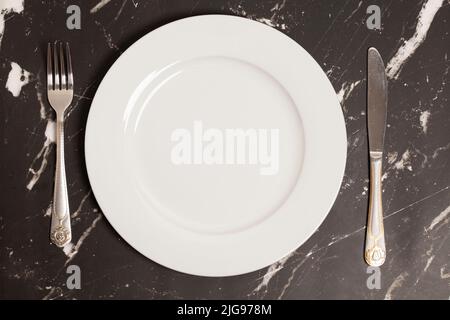 Knife and fork with plate on a marble background, top view Stock Photo