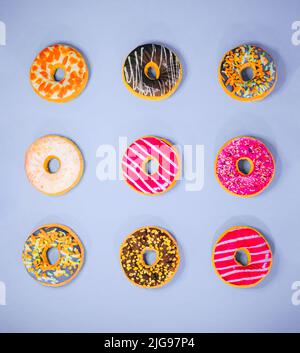 Set of 9 different colorful donuts isolated on purple background. In glaze, with chocolate, with sprinkles, topping, marshmallows, hazelnut. Minimal f Stock Photo