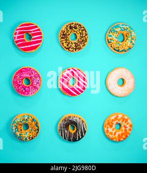 Set of 9 different colorful donuts isolated on blue background. In glaze, with chocolate, with sprinkles, topping, marshmallows, hazelnut. Minimal foo Stock Photo