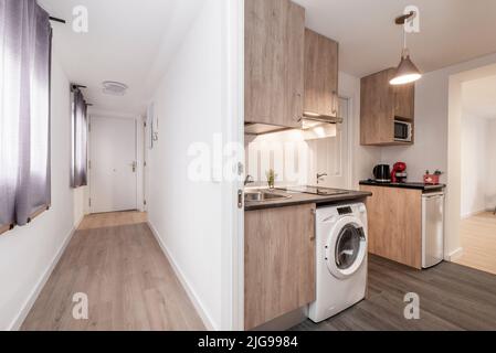 Corridor of a house with several doors and access to different rooms, open kitchen with oak furniture with white appliances Stock Photo