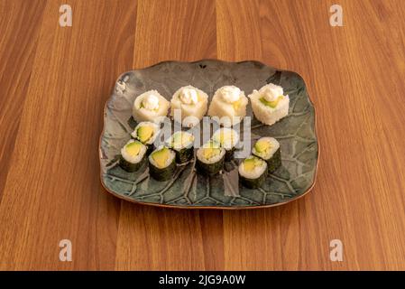 Porcelain tray with mixed avocado maki sushi and uramaki roll with sauce, white rice and nori seaweed Stock Photo