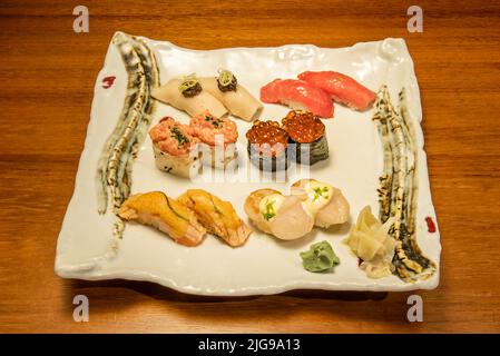 White porcelain tray with mixed roe gunkan sushi, marinated salmon nigiri, butterfish nigiri, scallops with maki and uramaki roll with sauce, white ri Stock Photo