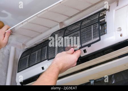 The man takes out filters from the air conditioner for cleaning. Split system maintenance. Stock Photo