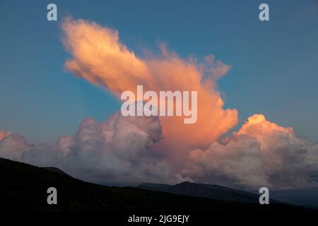 An orange cirro-cumulus and cumulus clouds in the evening light at sunset in the mountains Stock Photo