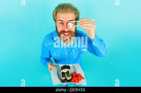 Bearded man eating sushi with chopsticks. Handsome male with plate of maki rolls. Japanese food. Stock Photo