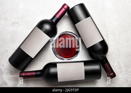 Cabernet Wine: Overhead view of a group of three bottles with blank labels arranged in a triangle with a glass of wine in the middle. Stock Photo