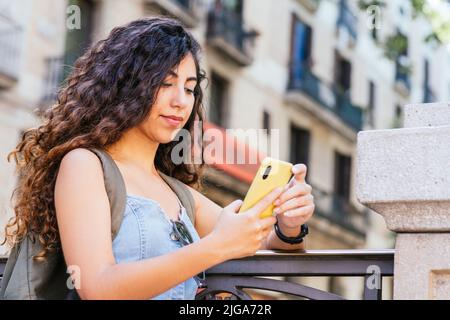 young turkish tourist with a pack pack checking her phone while leaning on a fence Stock Photo