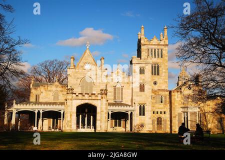 A young adult couple sits on the bench talking in front of the Lyndhurst Castle, historic home of financier Jay Gould, on a sunny day in Tarrytown, NY Stock Photo