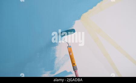 Decorator painting wall in blue color and using scotch tape Stock Photo