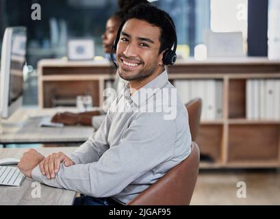 Here to provide quality service. a handsome young customer service agent sitting in the office and wearing a headset. Stock Photo