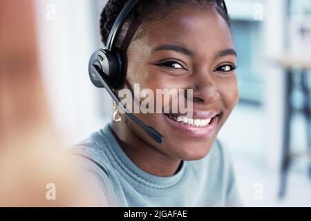 The office has the best lighting for selfies. an attractive young customer service agent sitting alone in the office and taking a selfie. Stock Photo
