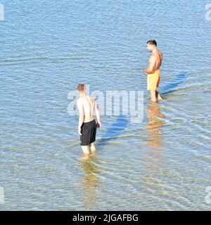 Boscombe, Bournemouth, Dorset, England, UK, 9th July 2022, Weather. Heatwave in mid-summer. People arrive at the beach before 8 am on Saturday morning. Temperatures will reach the high 20s by afternoon in wall-to-wall sunshine. Boys wading into the sea. Credit: Paul Biggins/Alamy Live News Stock Photo