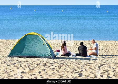 Boscombe, Bournemouth, Dorset, England, UK, 9th July 2022, Weather. Heatwave in mid-summer. People arrive at the beach before 8 am on Saturday morning. Temperatures will reach the high 20s by afternoon in wall-to-wall sunshine. People sitting on the beach with a tent. Credit: Paul Biggins/Alamy Live News Stock Photo