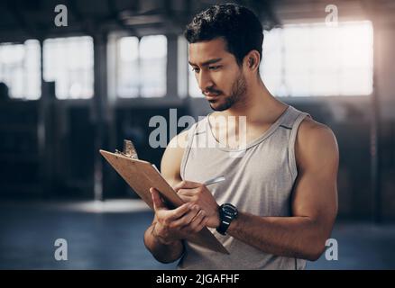 Checking up on his training inventory. a muscular young man writing notes on a clipboard while working in a gym. Stock Photo