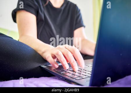 A closeup of female hands sitting on bed and typing on computer Stock Photo