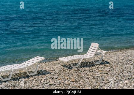 Pair of sun loungers at pebble beach, perfect vacation. Stock Photo