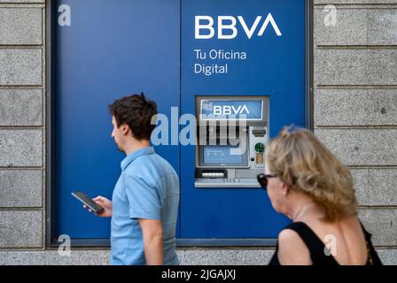 Pedestrians walk past an ATM machine at the Spanish multinational Banco Bilbao Vizcaya Argentaria SA (BBVA) bank branch in Spain. Stock Photo