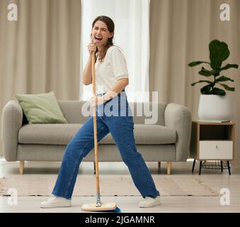 Fun was had. a young woman singing while sweeping the floors at home. Stock Photo