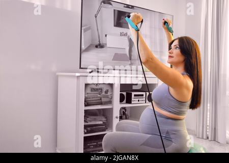 Pregnant young woman doing exercises and stretching at home. Stock Photo