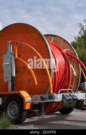 Large orange wooden spool for cable reel with red coiled electricity cable on a trailer outdoor Stock Photo