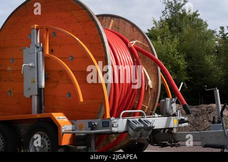Large orange wooden spool for cable reel with red coiled electricity cable on a trailer outdoor Stock Photo