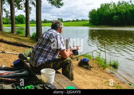 sunny photo from summer with an angler, angler sits on the shore of the lake and catches fish, Stock Photo