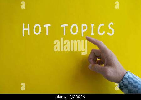 Hand pointing Hot Topics text on yellow cover background. Hot Topics concept Stock Photo