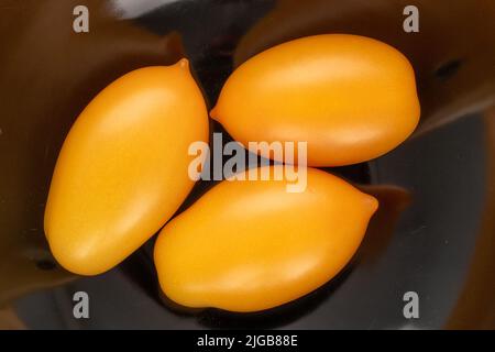 Three ripe yellow tomatoes on a black ceramic dish, close-up, top view. Stock Photo