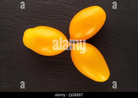 Three ripe yellow tomatoes on a slate stone, close-up, top view. Stock Photo