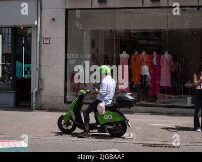 Antwerp, belgium, 02 July 2022, Man sits on a green electric scooter from Go Sharing and views the app on his smartphone Stock Photo