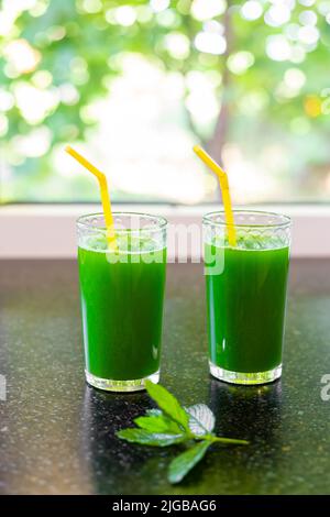 A green drink made from fresh vegetable greens with chlorophyll in glasses on the countertop, against the background of the window. Stock Photo