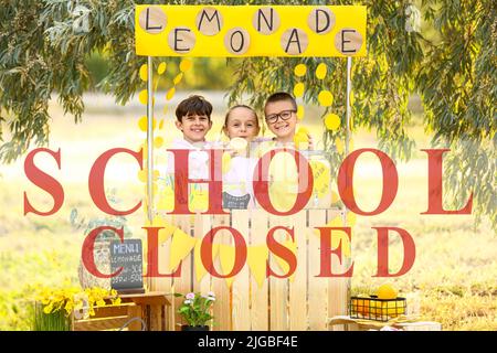 Text SCHOOL CLOSED and cute children selling lemonade in park Stock Photo