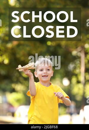 Text SCHOOL CLOSED and cute little boy playing with wooden airplane in park Stock Photo