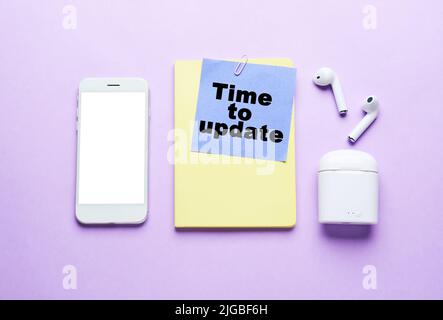 Smartphone, notebook, earphones and paper with text TIME TO UPDATE on lilac background Stock Photo