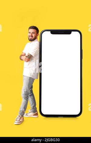 Cool tattooed young man near big smartphone on yellow background Stock Photo