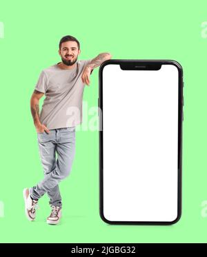 Cool tattooed young man near big smartphone on green background Stock Photo